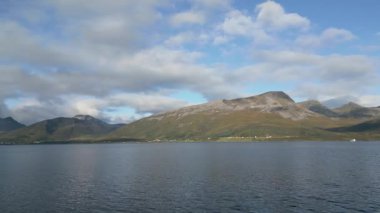 Sakin bir Norveç fiyordunun nefes kesici panoramik görüntüsü. Görkemli dağları ve dağılmış beyaz bulutları olan güzel bir gökyüzü..