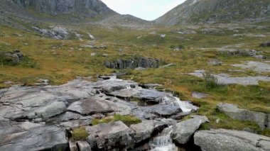 Bir hava aracı Norveç 'in Lofoten Adaları' ndaki engebeli bir vadiden akan güzel bir dağ deresini yavaşça ortaya çıkarıyor..