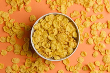 Turuncu arka planda beyaz kasede mısır gevreği. Sağlıklı kahvaltı manzarası. Sabah yemeği..