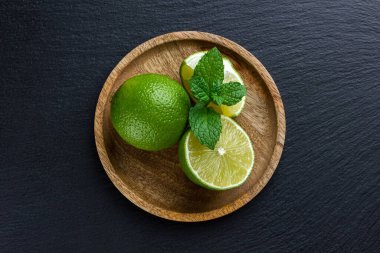 Koyu taş zemin üzerinde tahta tabakta naneli limonlar. Taze narenciye manzarası.