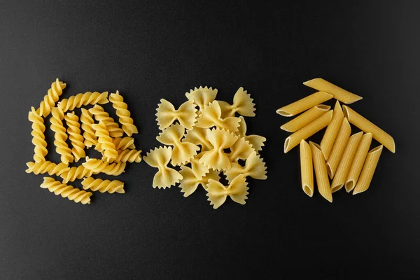 Different kinds of raw pasta with copy space on black background. Top view of Italian cuisine ingredient.