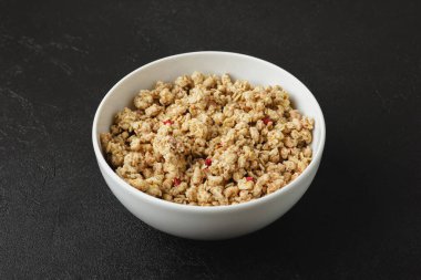 Granola in bowl on dark background. Healthy food on black table. Side view of homemade breakfast.