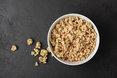 Granola in white bowl on dark table. Healthy food on black background. Top view of homemade breakfast.