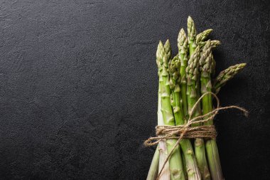 Green asparagus on a black background with copy space. Fresh and natural uncooked asparagus. Healthy plant food. Top view.