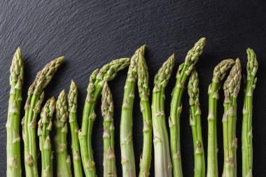 Green asparagus on a black background. Fresh and natural uncooked asparagus. Healthy plant food. Top view.