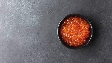 Red caviar in a black bowl. Sea food on a dark background with copy space. Top view.
