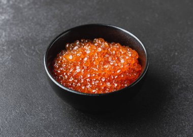 Salmon caviar in a bowl. Fresh sea food on a dark background. Side view.