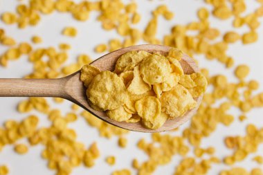 Corn flakes on wooden spoon white background. Top view of healthy breakfast.