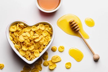 Corn flakes in heart bowl with honey on white background. Top view of healthy breakfast.
