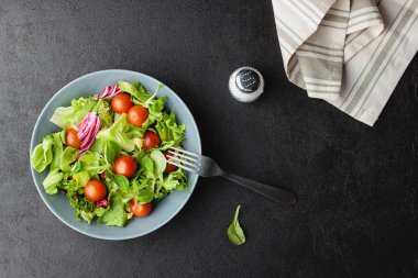 Yeşil salata yaprakları ve siyah masada kiraz domatesleri. Taze ve sağlıklı yiyecekler. Üst görünüm.