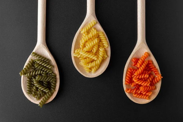 Raw pasta torti on wooden spoons on black background. Top view of Italian cuisine ingredient.