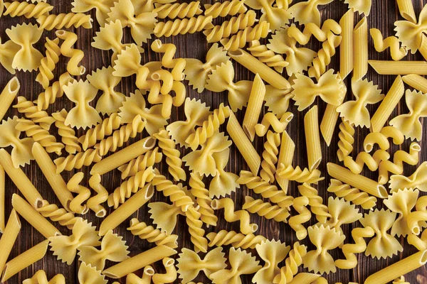 Different kinds of raw pasta texture on wooden background. Top view of Italian cuisine ingredient.