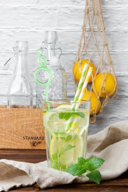 Bardakta naneli limonata, şebeke çantasında limonlar ve tahta masada şişeler. Taze narenciye manzarası.