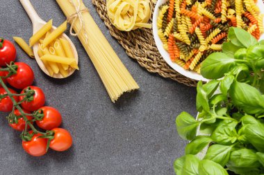 Spagetti, tagliatelle, penne ve vişneli domates ve fesleğenli çiğ makarna. Üst görünüm.