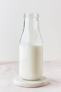 Masanın üzerinde bej masa örtüsü ve mermer tezgahı olan bir şişe taze süt. Sağlıklı bir içki. Kalsiyum ve vitamin kaynağı. Yan görünüm.