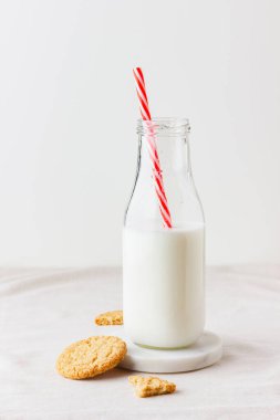 A bottle of fresh milk with oatmeal cookies on a table with a beige tablecloth. Healthy food for breakfast or snack. Side view.