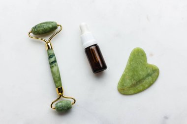 Yeşil yeşim silindir ve beyaz mermer üzerinde yüz için gua sha masaj aleti. Moda bir kozmetik alet. Yaşlanma karşıtı terapi. Üst Manzara. Düz yatıyordu. Boşluğu kopyala.