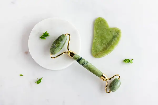 stock image Green jade roller and gua sha massager for face on white marble. Trendy cosmetic tool. Anti aging therapy. Top view. Flat lay. Copy space.