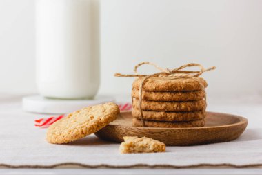 Oatmeal cookies are tied with craft thread on a wooden plate. Healthy food for breakfast or a snack with milk. Side view. Copy space.