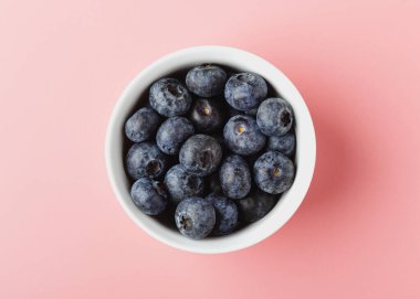 Pembe arka planda beyaz kasede yaban mersini. Taze organik böğürtlen manzarası.