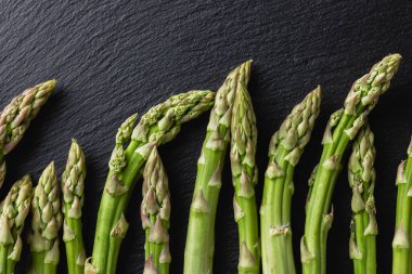 Green asparagus on a black background. Fresh and natural uncooked asparagus. Healthy plant food. Top view.