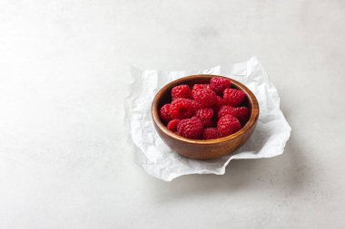 Açık gri arka planda ahşap bir kasede ahududu. Taze kırmızı meyveler..