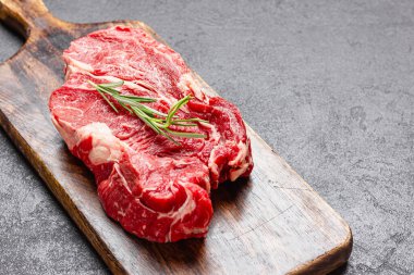 Tahta kesme tahtasının üzerinde pişmemiş büyük bir parça kırmızı et. Koyu arkaplanda biberiyeli çiğ et..