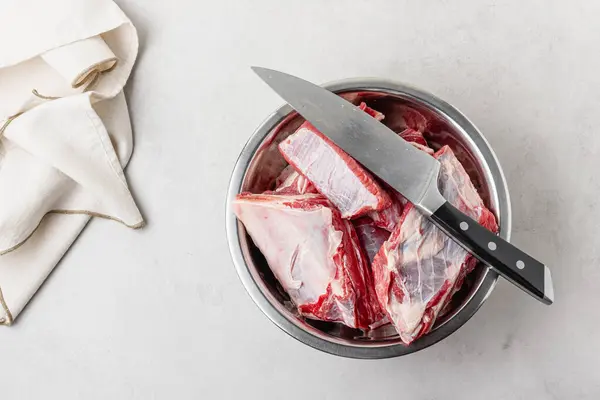 stock image Raw beef ribs in bowl with big knife. Pieces of fresh uncooked red meat on grey background.