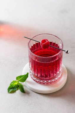 Mermer tezgahta bir bardakta ahududu kokteyli ve arka planda taze nane şekeri. Yaz kırmızı içeceği.