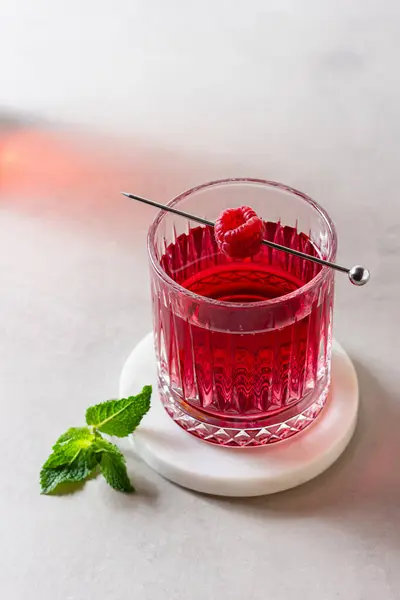 Mermer tezgahta bir bardakta ahududu kokteyli ve arka planda taze nane şekeri. Yaz kırmızı içeceği.
