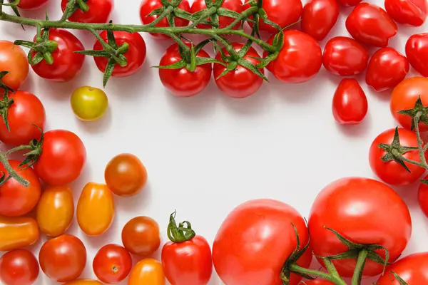 Variety of tomatoes on white background with copy space. Frame composition. Fresh vegetables. Top view.