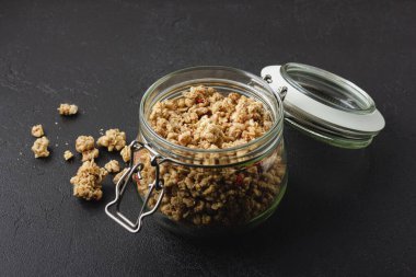 Kavanozda granola. Siyah masada ev yapımı sağlıklı bir kahvaltı. Yan yemek..