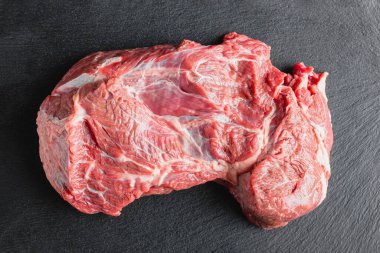 Siyah servis tabağında çiğ et. Koyu arkaplanda pişmemiş büyük bir parça kırmızı et..