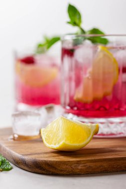 Ahşap kesme tahtasındaki buzlu ahududu kokteyli. Hafif arka planda naneli ve limonlu ferahlatıcı bir meyve suyu. Ayrıntıları kapat.