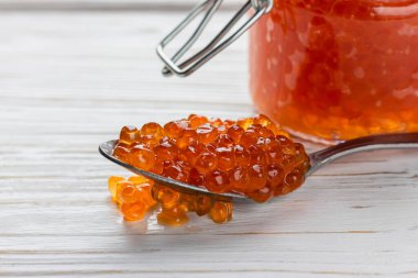 Kırmızı havyar kaşıkta. Deniz ürünleri beyaz ahşap masaya yakın. Lüks somon lezzeti. Yan görünüm.