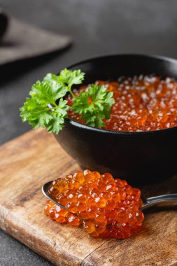 Gümüş kaşıkta maydanozlu havyar. Karanlık bir arka planda siyah bir kasede deniz mahsulleri. Tahta kesme tahtasındaki lüks lezzet. Yan görünüm.