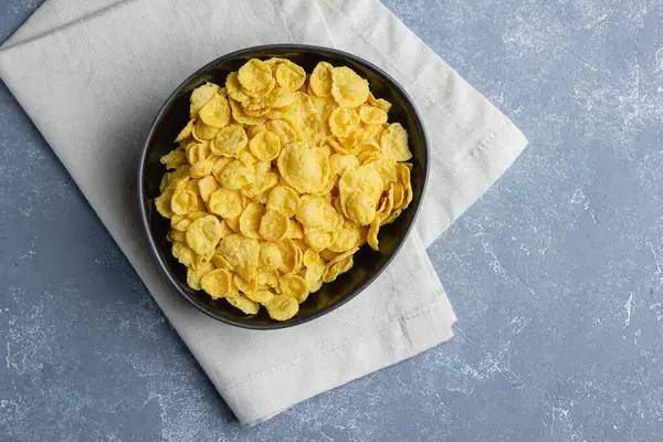 stock image Corn flakes in black bowl on blue background.