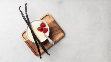 Beyaz kasede ahududulu vanilyalı puding. Tahta tepside tatlı.