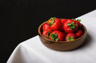 Tahta kasede çilek. Beyaz masa örtüsünde kırmızı böğürtlen ve siyah duvar. Sağlıklı ve organik tatlı..