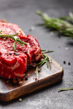 Tahta kesme tahtasında çiğ et. Büyük bir parça pişmemiş kırmızı et ve koyu arkaplanda biberiye..