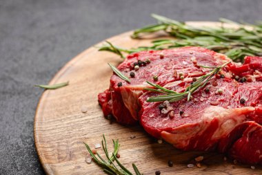 Büyük bir parça pişmemiş kırmızı et ve koyu arkaplanda biberiye. Tahta tepside çiğ et.