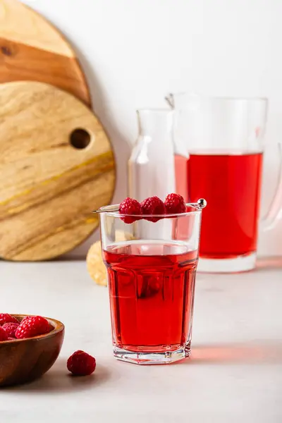 Gri arka plandaki bardakta ahududu içeceği var. Sürahide çilekli limonata. Yan görünüm.