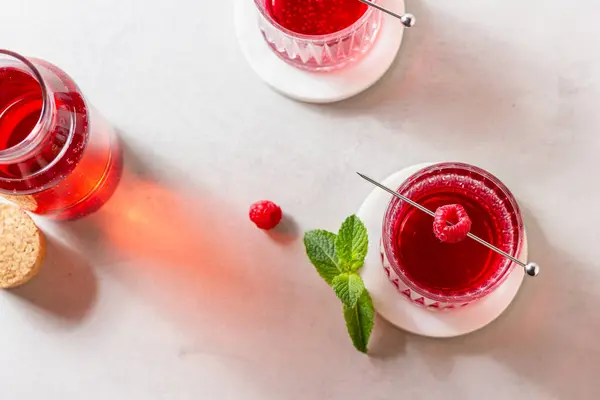Mermer tezgahta bir bardakta ahududu kokteyli ve arka planda taze nane şekeri. Yaz kırmızı içeceği.