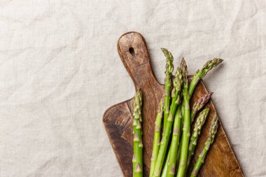 Keten masa örtüsünün üzerindeki tahta kesme tahtasındaki yeşil kuşkonmaz. Taze ve doğal pişmemiş kuşkonmaz. Sağlıklı bitki yiyeceği.