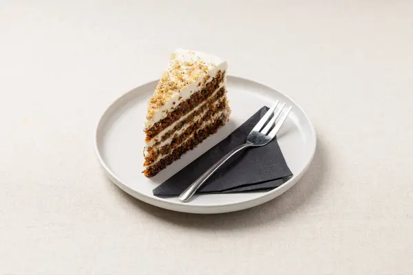 Beyaz tabakta bir parça havuçlu turta. Masada bej masa örtüsü olan lezzetli bir tatlı..