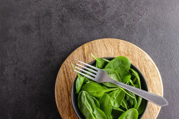Taze yeşil ıspanak yaprakları kasede. Siyah masada doğal vejetaryen yemekleri..
