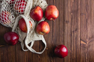 Ahşap bir arka planda şebeke çantasındaki kırmızı elmalar. Kopya alanı olan taze meyvelerin üst görünümü.