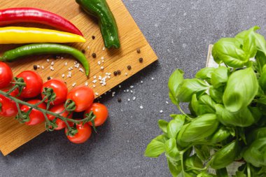 Acı biberli kiraz domatesleri ve ahşap kesim tahtasında baharatlar ve yeşil fesleğen. Taze sebzeler ve bitkiler. Sağlıklı organik gıdaların en üst görüntüsü.