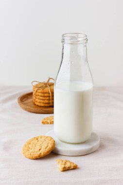 A bottle of fresh milk with oatmeal cookies on a table with a beige tablecloth. Healthy food for breakfast or snack. Side view.