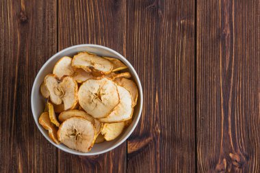 Tahta bir masada, beyaz bir kasede kurutulmuş elma..